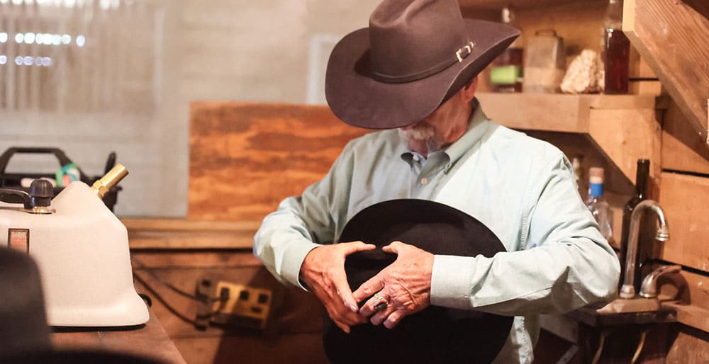 Un vaquero con un sombrero negro, sosteniendo y dando forma a un sombrero negro.